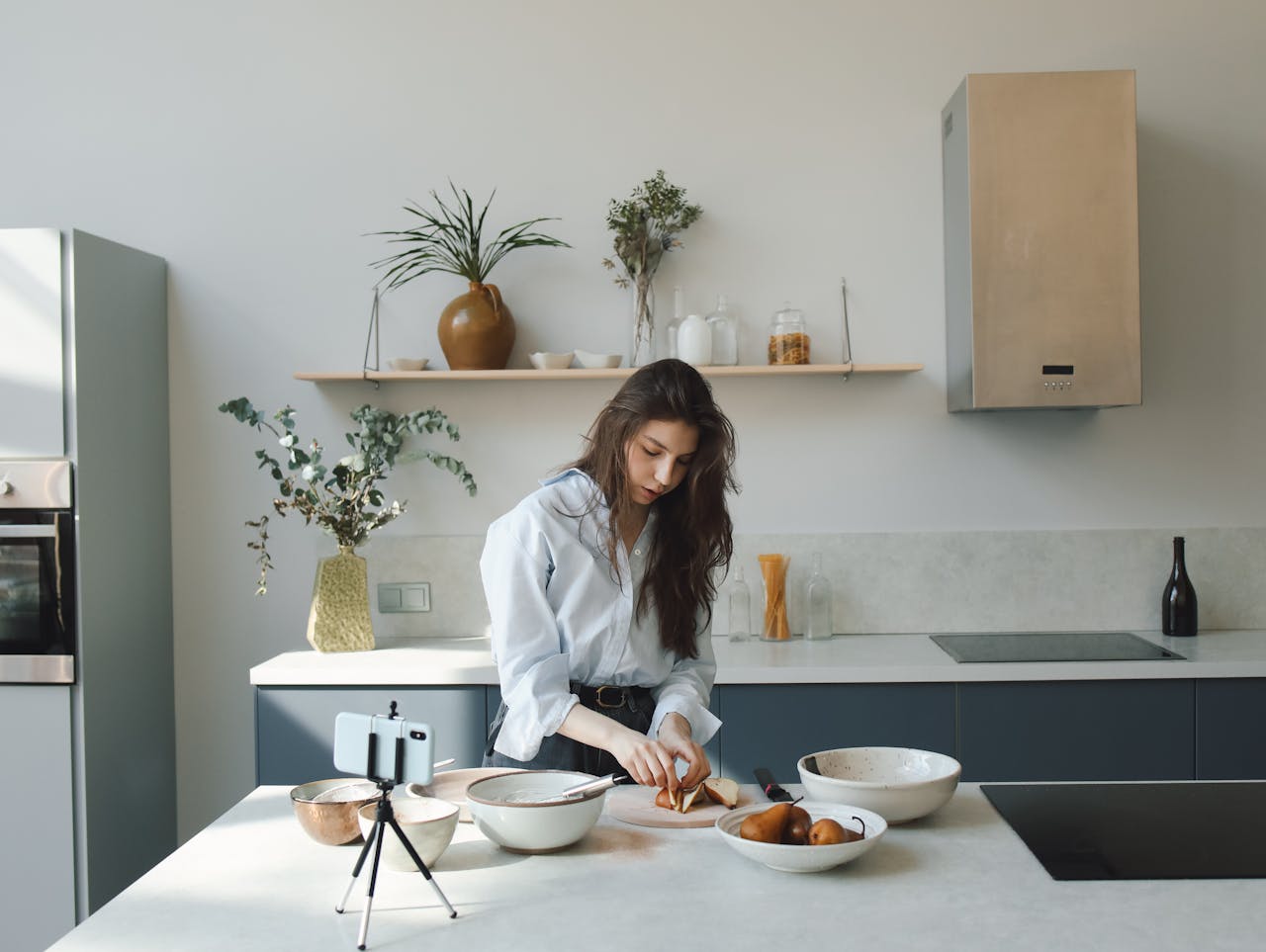 A young woman prepares food while recording a cooking video in a stylish kitchen.